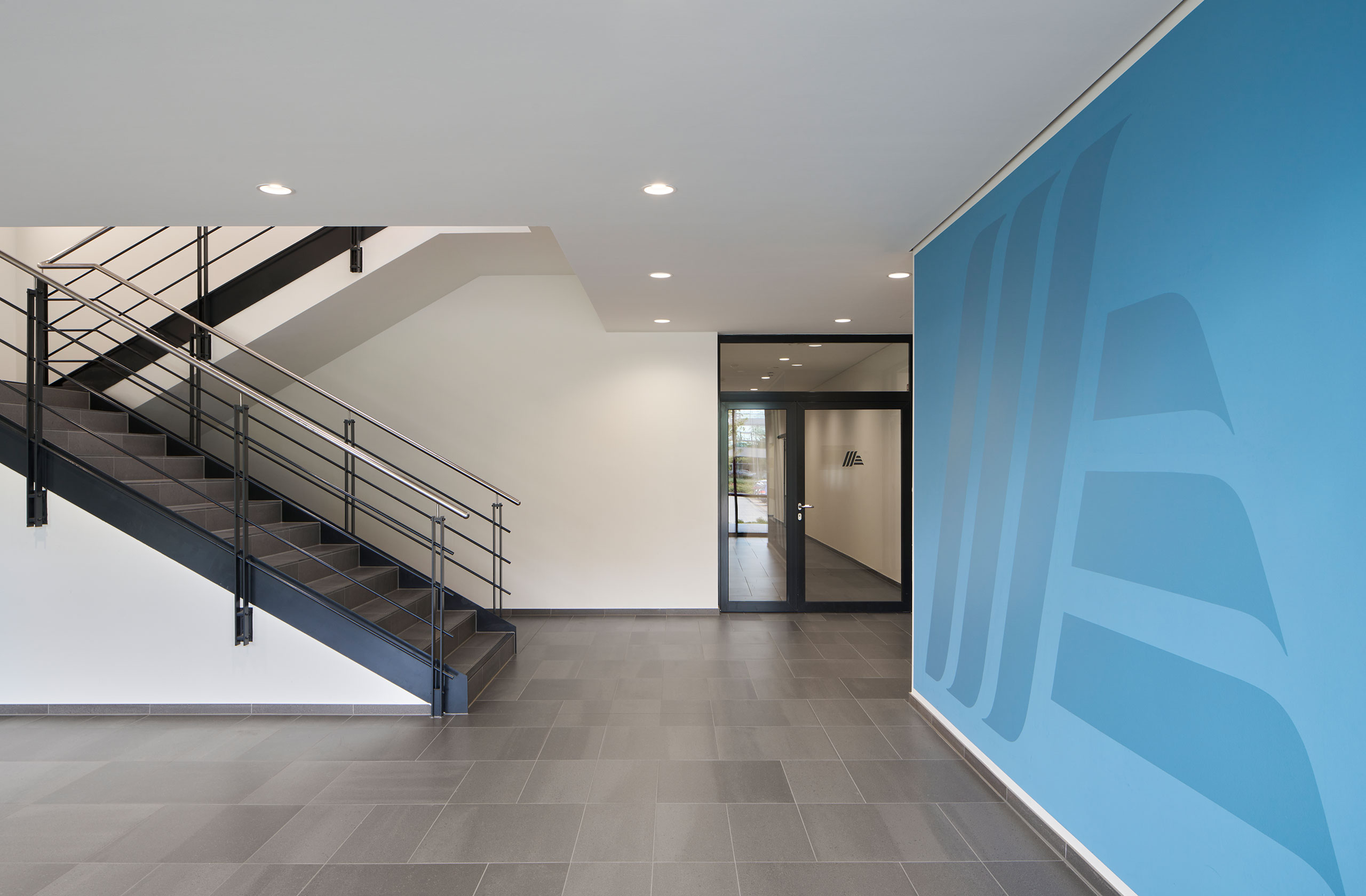 Foyer mit offener Treppe und blauer Akzentwand mit Aldi Logo