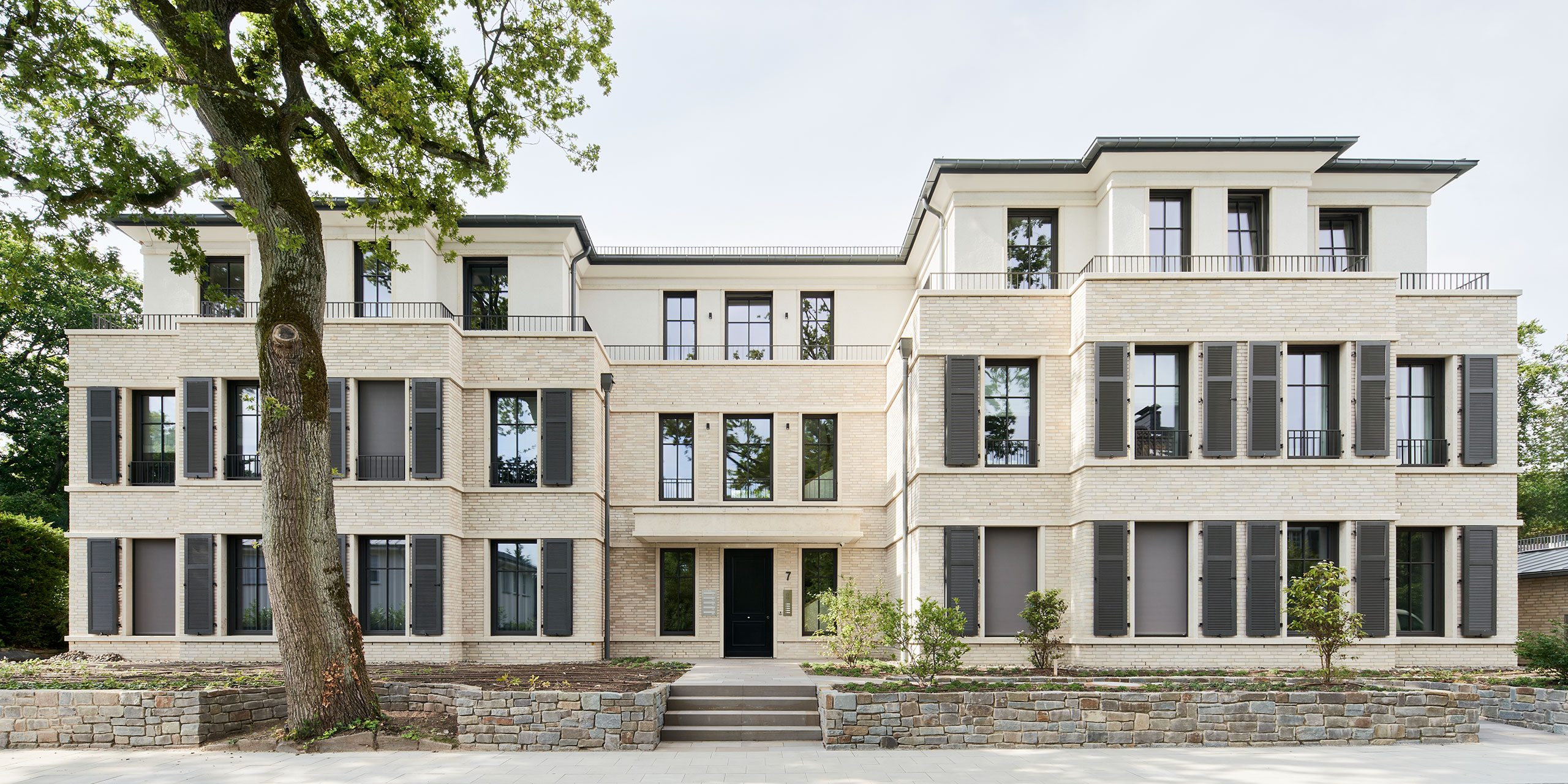 Gesamtansicht der Wohnbebauung mit hellem Klinker, Natursteinsockel und großzügigen Fensteröffnungen