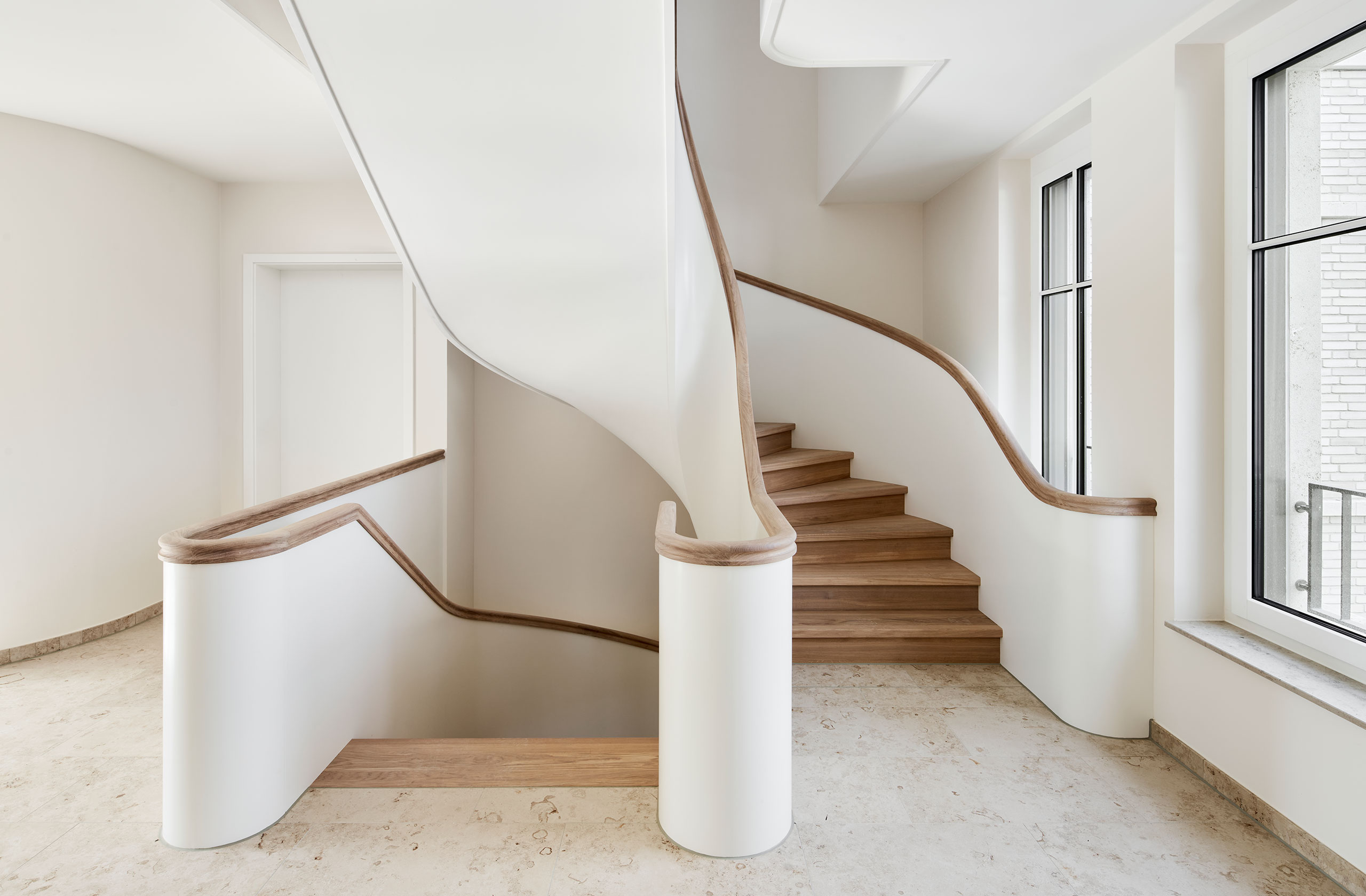 Lichtdurchflutetes Treppenhaus mit geschwungener Treppe und Holzhandlauf