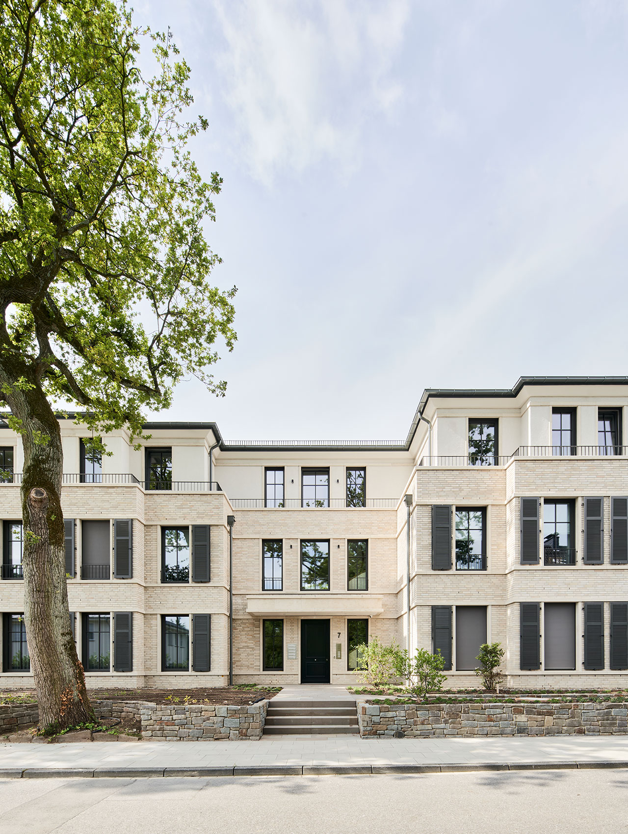Straßenansicht des Mehrfamilienhauses mit hellem Klinker und bestehendem Baumbestand