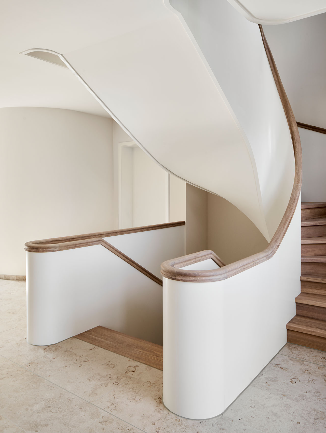 Geschwungene Treppe mit weißem Geländer und Holzhandlauf