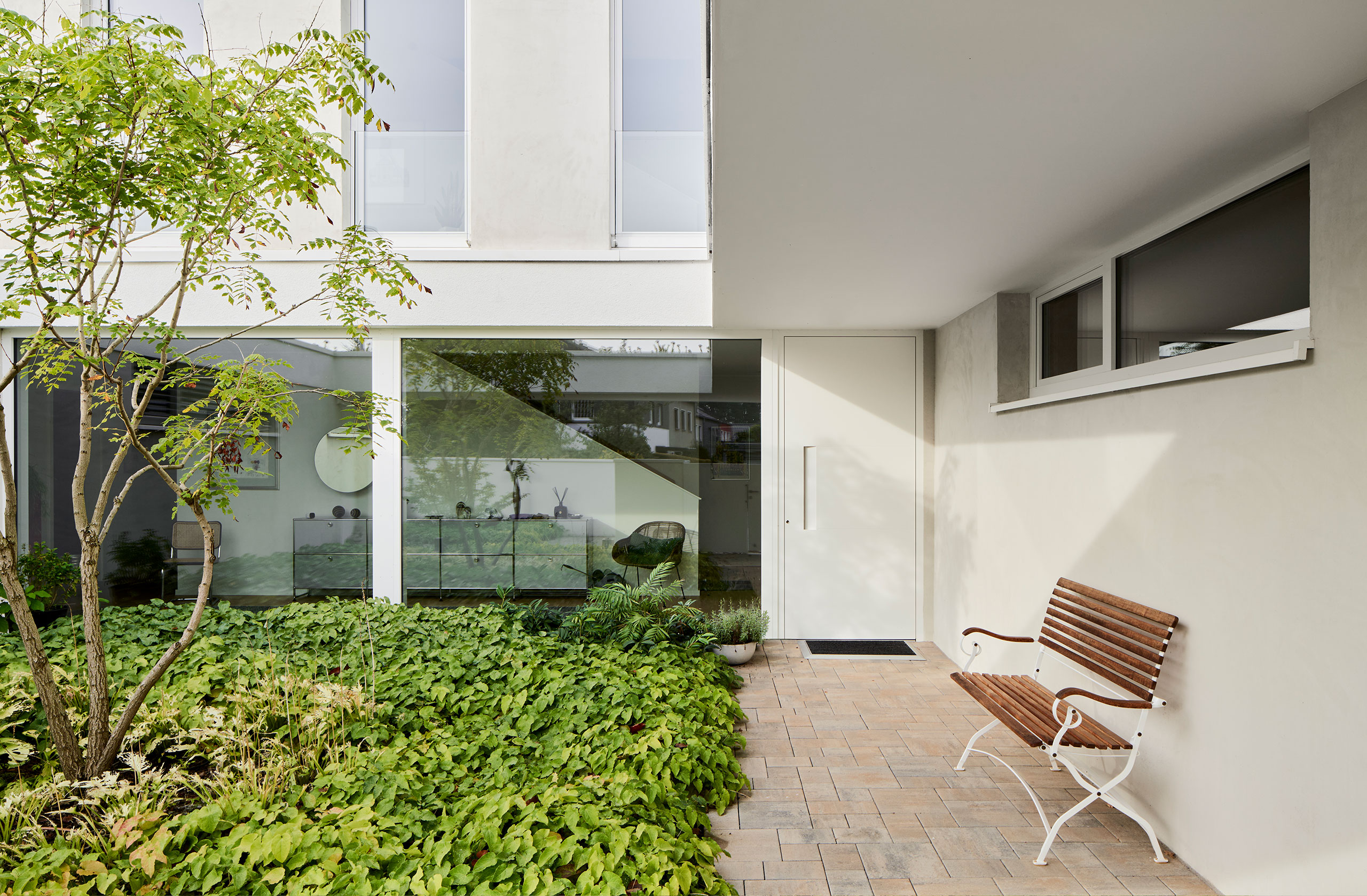 Überdachter Sitzbereich im begrünten Innenhof eines modernen Wohnhauses mit Einliegerwohnung