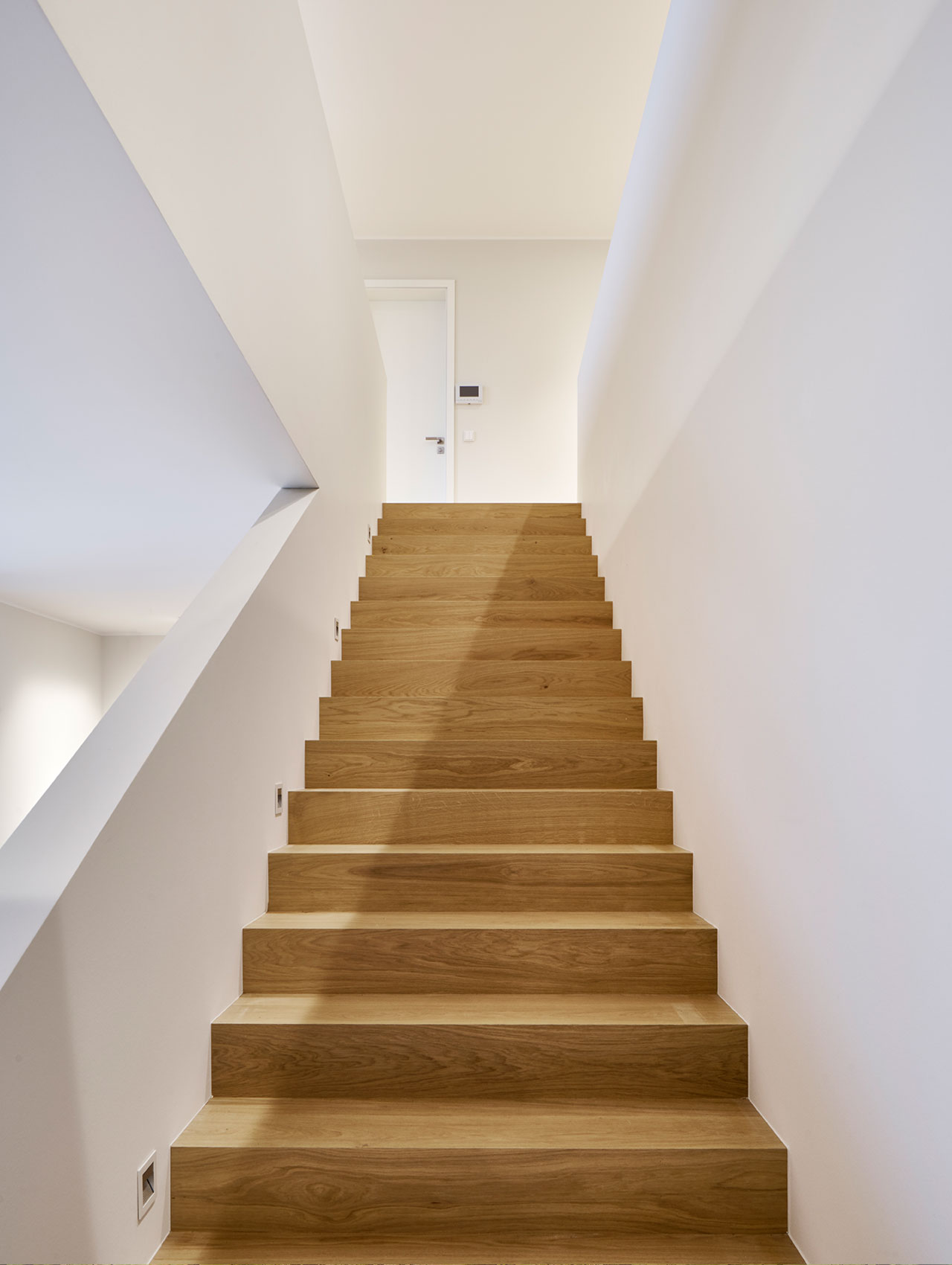 Innenraum mit geradläufiger Holztreppe und weißem Wandverlauf