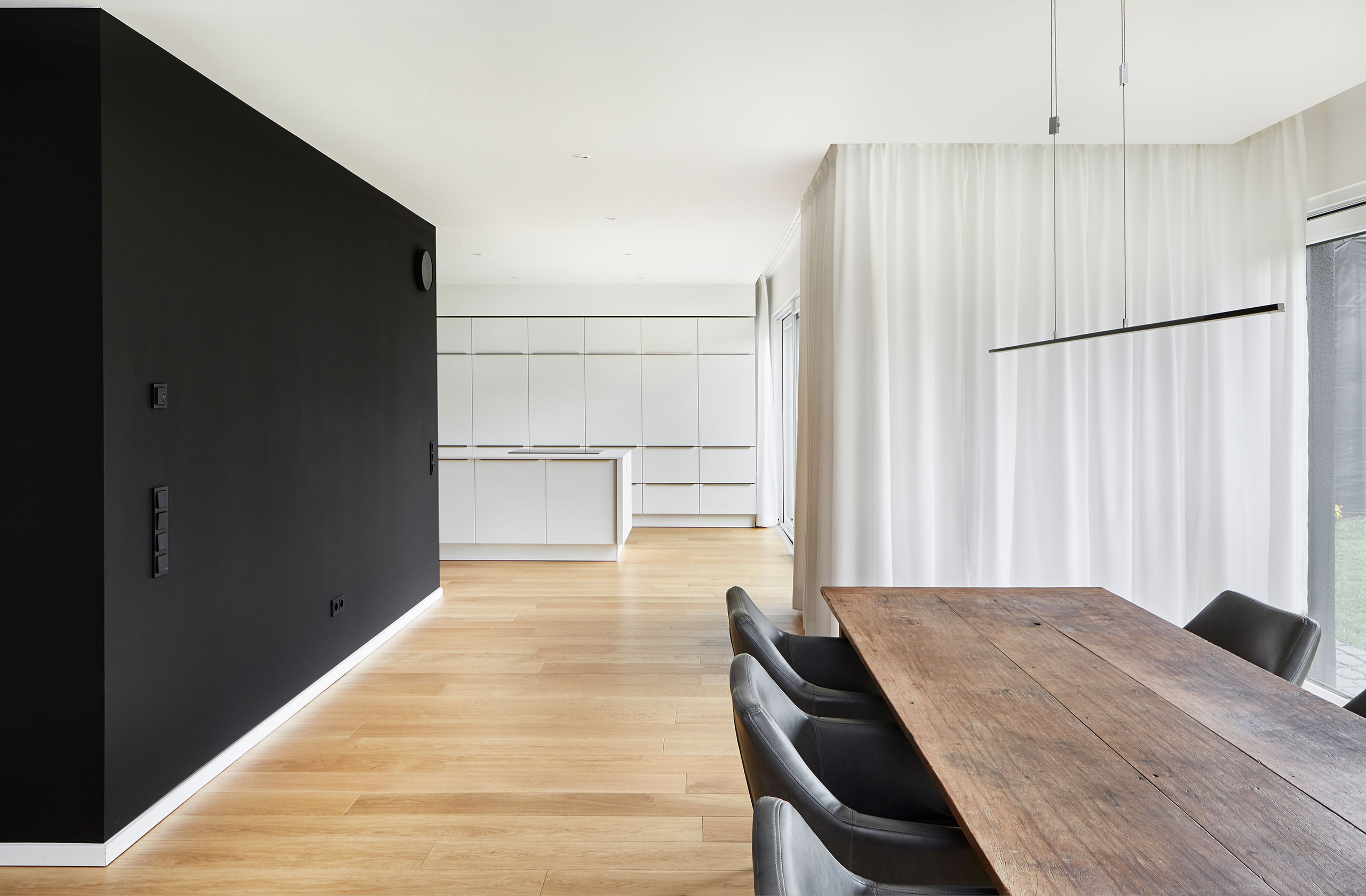 Essbereich mit massiver Holztafel, schwarzer Wand und offener Küche