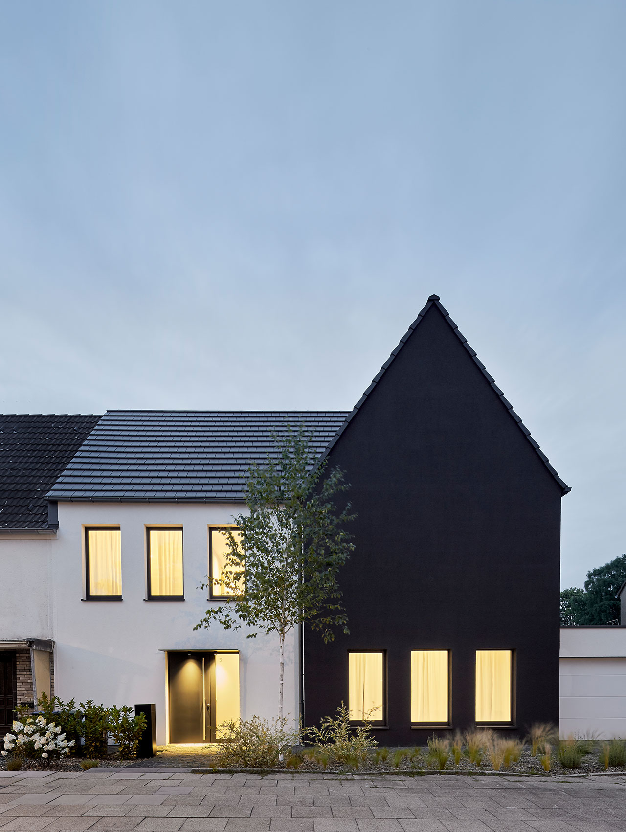 Frontansicht des Wohnhauses bei Abendlicht mit beleuchteten Fenstern