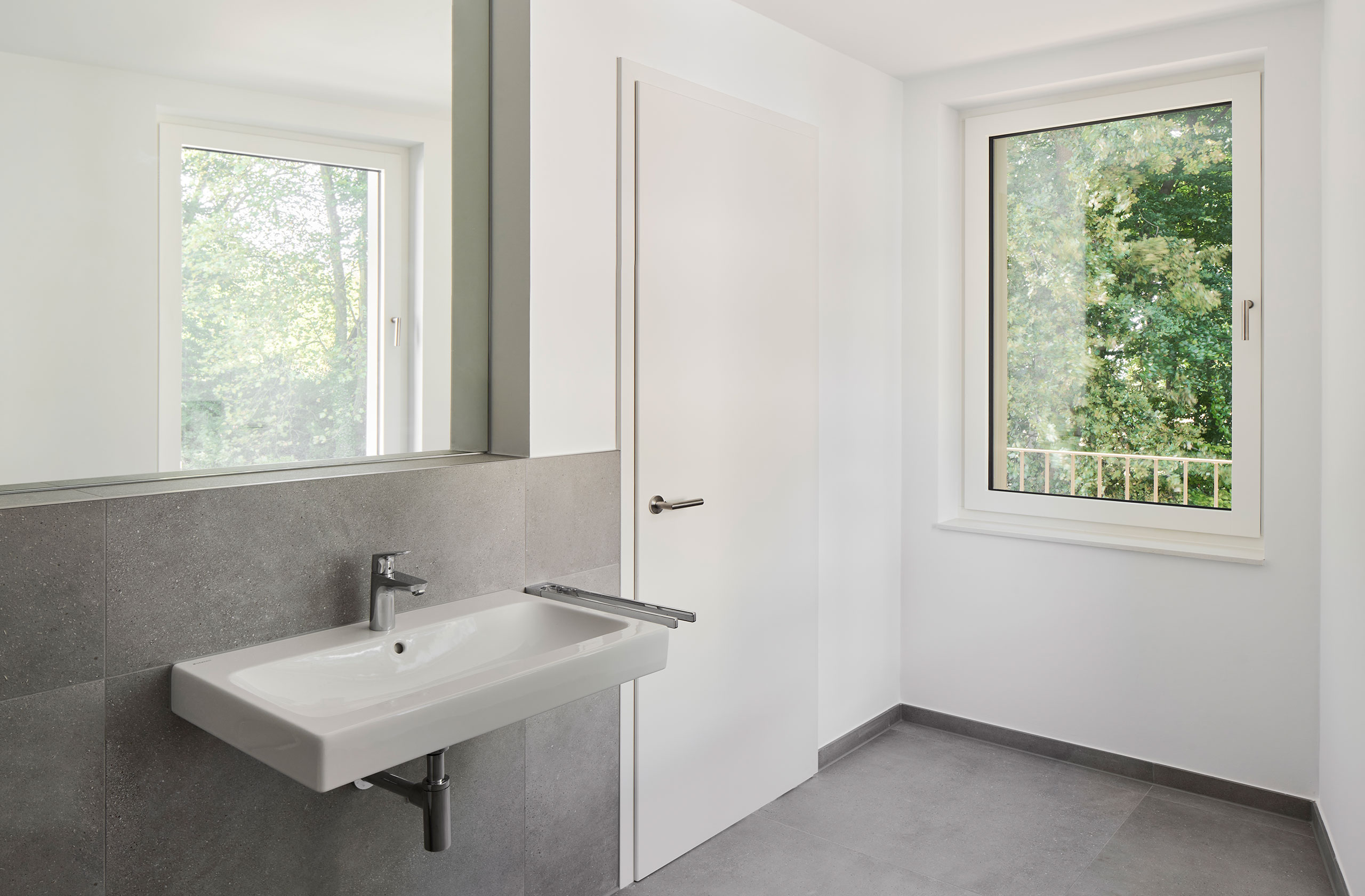 Badezimmer mit Fenster, grauen Fliesen und schlichtem Waschtisch