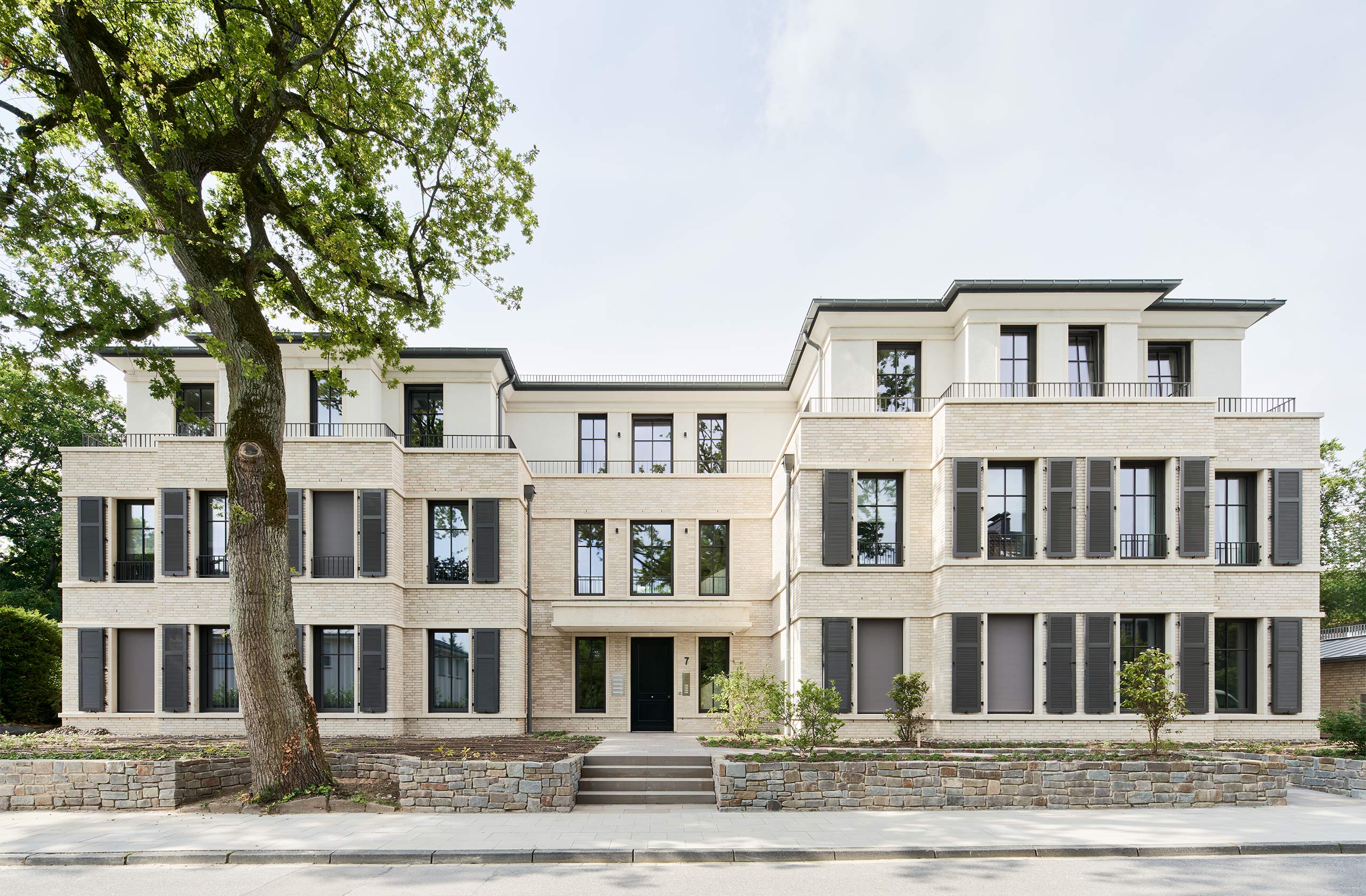 Gesamtansicht der Wohnbebauung mit hellem Klinker, Natursteinsockel und großzügigen Fensteröffnungen
